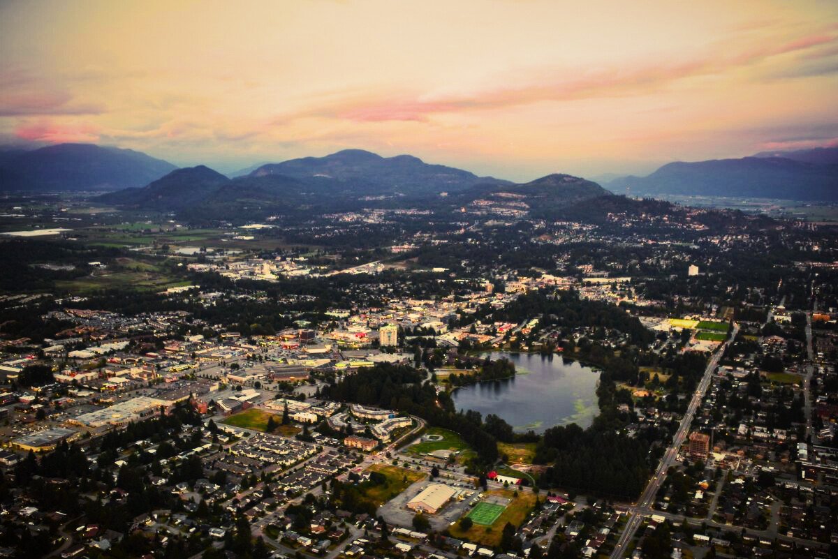 An aerial view of a city with a lake, surrounded by mountains and a colorful sunset sky.